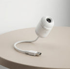 A compact and portable white mini galaxy star projector featuring a flexible neck and USB connector from Dreams Setup, resting on a minimalist desk.